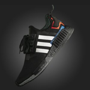 Close-up photo of a black Adidas NMD sneaker with detailed textures on a dark background.